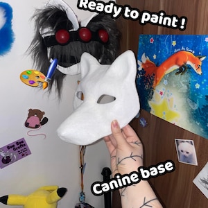 Op de afbeelding: Een wit canine basismasker, met de tekst "Canine base". Het masker is klaar om te worden geverfd. Andere items zijn een Pikachu-knuffel, een kunstdruk van een vos en een zwart-grijs masker. De tekst "Ready to paint!" is ook aanwezig.