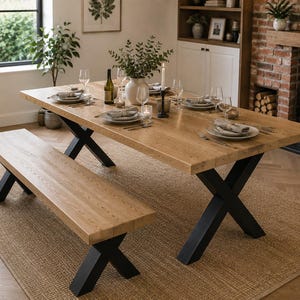 May include: A rectangular dining table and a matching bench, both featuring thick light brown wooden tops with visible grain and sturdy black metal X-shaped legs. The table is set with white plates, glassware, silverware, and a central vase.