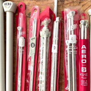 May include: A selection of AERO knitting needles in clear plastic packaging with red backing. The needles are silver-coloured, with white tops. Sizes include 4, 7, 9, and 11. The packaging includes text that reads "MADE IN ENGLAND". The 3.5mm needles are also shown.