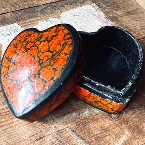 May include: A black heart-shaped box with an orange and black floral design. The box is open and the inside is empty.
