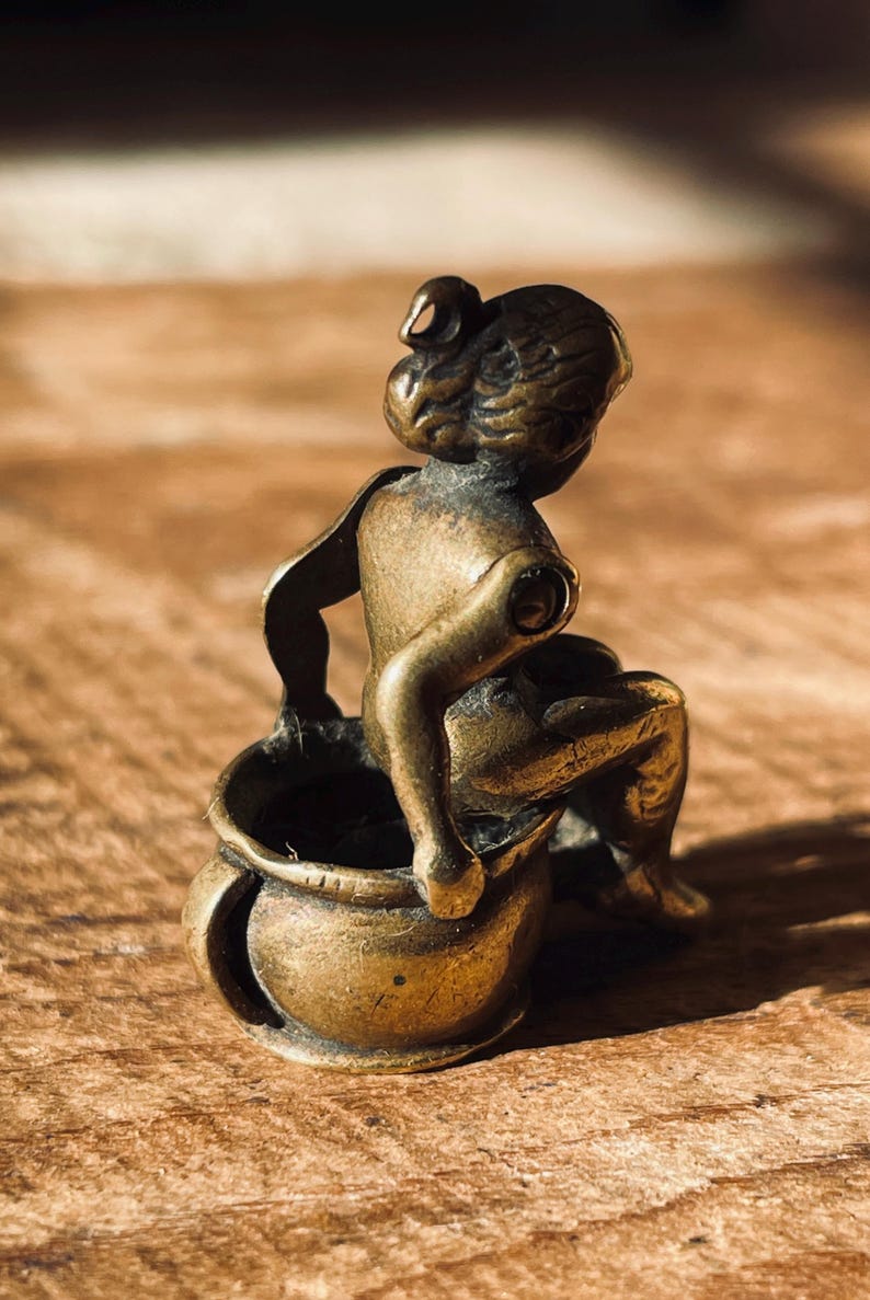 Pu&ograve; includere: Una piccola statuetta di bronzo di una persona seduta su un vaso. La statuetta &egrave; dettagliata e ha un aspetto realistico.