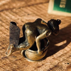 Pu&ograve; includere: Una statuetta in ottone di una persona che si piega su un piccolo vaso. La statuetta &egrave; un aprilettere in stile vintage.