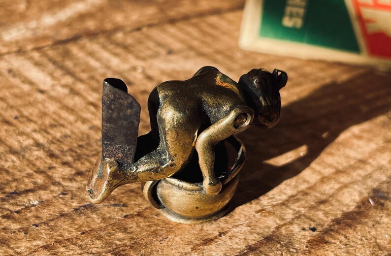 Pu&ograve; includere: Una statuetta in ottone di una persona che si piega su un piccolo vaso. La statuetta &egrave; un aprilettere in stile vintage.