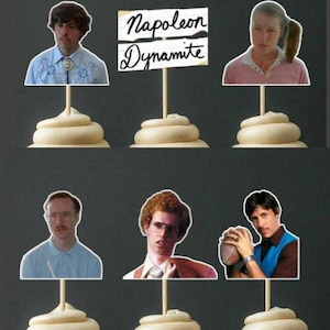 May include: Cake toppers featuring characters from the movie "Napoleon Dynamite." The toppers include images of the characters and a sign that reads "Napoleon Dynamite." Each topper is attached to a swirl of frosting.