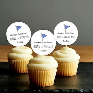 May include: Three cupcakes with white frosting and blue and white circular toppers that say "Marked Safe From Being Intoxicated Today".