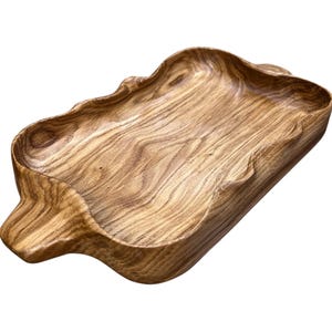 May include: A rectangular wooden tray featuring a natural light and dark brown wood grain pattern. The tray has an organic, wavy edge design with two integrated handles on the shorter sides, showcasing a smooth, polished finish throughout.