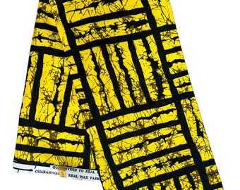 May include: A folded fabric with a bold geometric pattern in black and yellow. The design features thick black lines forming rectangular shapes against a bright yellow background. The fabric has text that reads "GUARANTEED FD REAL REAL WAX FABRIC".