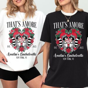 May include: White and black t-shirts with the text "THAT'S AMORE" above a heart-shaped design featuring raccoons, roses, and the text "Amelia's Bachelorette, New York, NY, EST. 2025".