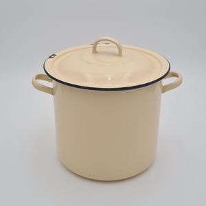 Peut inclure: Marmite en émail crème avec couvercle assorti. La marmite a deux poignées latérales et une poignée en boucle sur le couvercle. Le bord de la marmite et du couvercle est bordé de noir. Un article de cuisine classique.