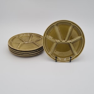 May include: A collection of olive green divided serving dishes. Each plate is round with five sections. A stack of plates is on the left, and a single plate is on a black stand on the right. The plates are ceramic.
