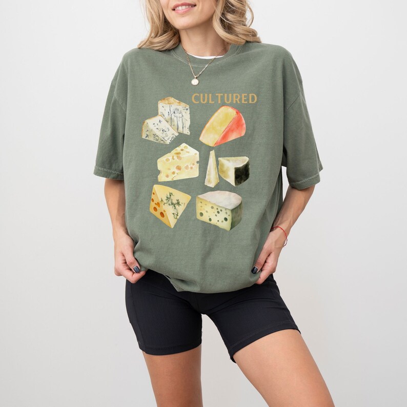 May include: A green t-shirt with a graphic of different types of cheese and the word "CULTURED" printed in gold.