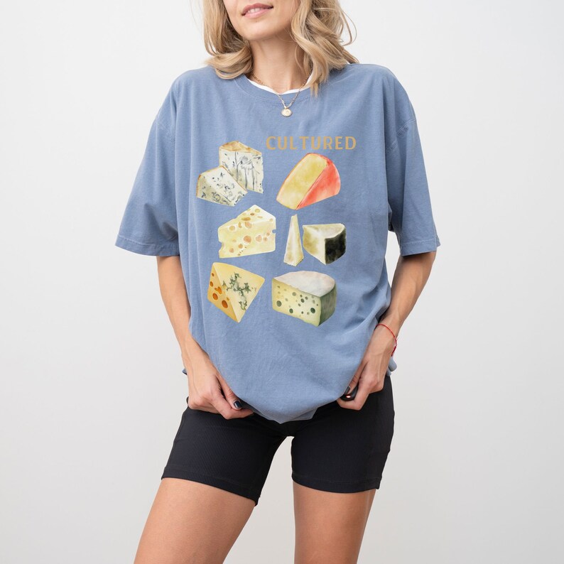 May include: A light blue t-shirt with a graphic of different types of cheese and the word "CULTURED" printed in gold lettering.