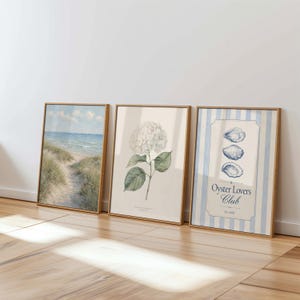 May include: Three framed art prints. One depicts a beach scene, another a botanical illustration of a hydrangea, and the third features oysters and the text "Oyster Lovers Club" on a blue and white striped background.