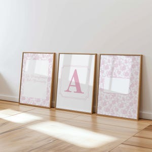 May include: Three framed wall art prints with light wood frames. The left print features a pink floral pattern with the text The Pennsylvania State University. The center print shows a large pink letter A. The right print displays a pink floral pattern.