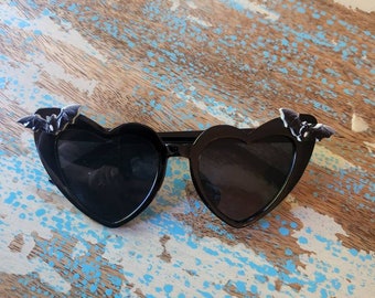 Puede incluir: Gafas de sol negras en forma de corazón con detalles de murciélago en las patillas.
