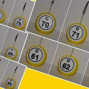 May include: A set of 12 yellow and white round table number holders with black numbers from 61 to 75. Each holder has a silver clip on top.
