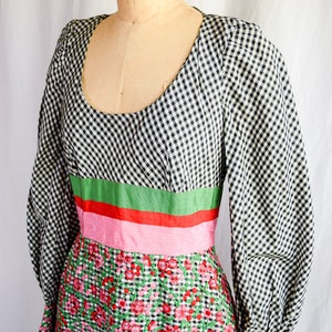 Pode incluir: Um vestido de vichy preto e branco com uma faixa verde, vermelha e rosa na cintura. A parte inferior do vestido é bordada com flores rosa e vermelhas.