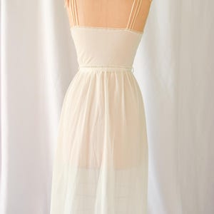 K&ouml;nnte beinhalten: Ein wei&szlig;es Schlupfkleid mit einem gewellten Saum und d&uuml;nnen Tr&auml;gern. Das Kleid hat ein tailliertes Oberteil und einen flie&szlig;enden Rock.