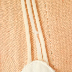 K&ouml;nnte beinhalten: Nahaufnahme eines wei&szlig;en Spitzenoberteils mit einem wei&szlig;en Stoffband. Das Band ist umgeklappt und hat eine ausgefranste Kante.