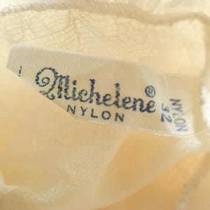K&ouml;nnte beinhalten: Ein wei&szlig;es Nylon-Etikett mit dem Text "Michelene" und "Nylon 32" in blauer Schrift.