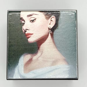 May include: A vintage-style illustration of a woman with dark hair and a white dress. The image is printed on a wooden box with a black frame.