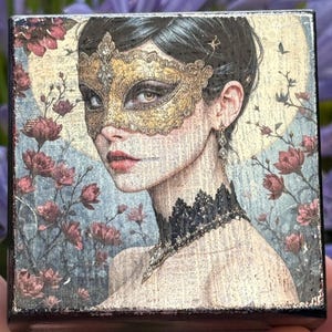Könnte beinhalten: Quadratischer Kunstdruck mit einer Frau, die eine goldene Maske und einen schwarzen Spitzen-Choker trägt. Das Kunstwerk hat eine Vintage-Ästhetik mit einem floralen Hintergrund in Rosa- und Blautönen. Die Frau hat dunkles Haar und roten Lippenstift.