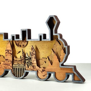 May include: A wooden train-shaped decorative piece with a layered design. The piece features a detailed depiction of a castle scene, with a warm, golden-brown background and a gray border. The design includes intricate cutouts and a layered effect.