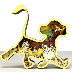 Puede incluir: Una escultura de madera multicapa con forma de león, que presenta personajes y escenas de una popular película de animación. La escultura tiene un contorno amarillo y representa personajes en un colorido entorno selvático.