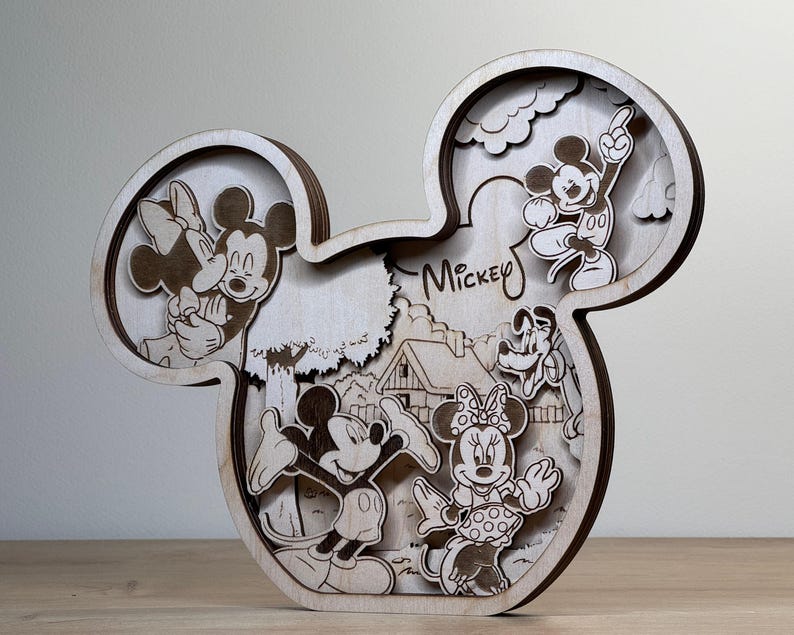 May include: Wooden Mickey Mouse-shaped wall art featuring layered cutouts of Mickey, Minnie, and other Disney characters. The word "Mickey" is written in script. The art piece is made of light-colored wood and has a three-dimensional effect.