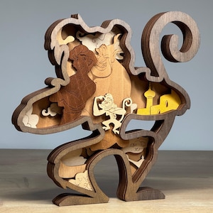 May include: A multi-layered wooden sculpture featuring characters from a popular animated film. The sculpture showcases Aladdin, Genie, Abu, and a yellow palace. The artwork is crafted from various shades of wood, creating a 3D effect.