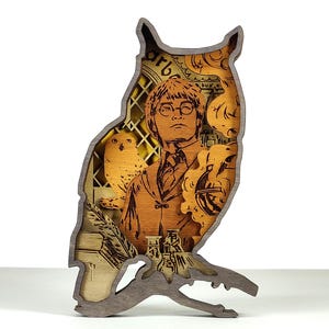 Può includere: Un'opera d'arte in legno a forma di gufo, con un design a strati che raffigura una persona, un gufo e altri elementi dettagliati. L'opera è principalmente nei toni del marrone e del beige, con dettagli intricati e una finitura strutturata. La sagoma del gufo è una caratteristica chiave.
