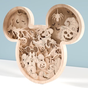 Pode incluir: Decoração de Halloween em madeira em forma da cabeça do Mickey Mouse. O design em camadas apresenta imagens esculpidas de Mickey, Minnie, Donald, abóboras, morcegos e uma aranha. A madeira castanha clara cria um efeito dimensional.