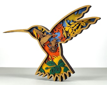 May include: A layered wooden hummingbird sculpture with a natural wood finish. The design features two hummingbirds, autumn leaves, and flowers in shades of orange, yellow, and blue. The sculpture is a decorative item.
