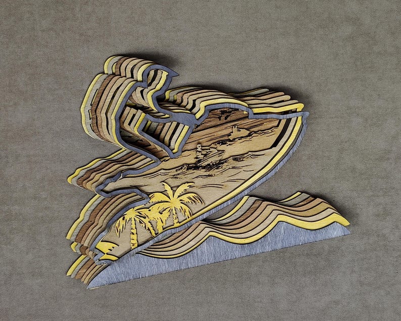 Pu&ograve; includere: Un'opera d'arte in legno a strati raffigurante un surfista su un'onda. L'opera presenta una tavola da surf, palme e un surfista. Il pezzo &egrave; realizzato con varie tonalit&agrave; di legno, con accenti gialli e grigi, creando un effetto 3D.