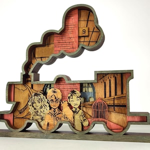 May include: A wooden train-shaped decorative piece featuring a scene with three cartoon characters, a birdcage, and a brick wall. The train is made of layered wood with a green frame and red and brown interior details. The number 9 is visible.