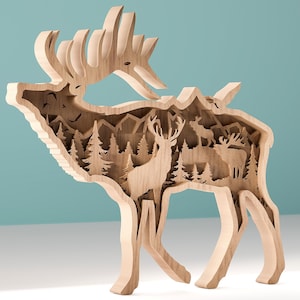 May include: A wooden elk sculpture with a layered design. The elk's silhouette frames a detailed forest scene with trees, mountains, and other elk. The sculpture is made of light-colored wood and stands on a white surface against a teal background.