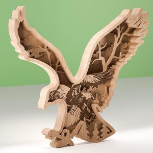 Może przedstawiać: Drewniana rzeźba orła z rozpostartymi skrzydłami, prezentująca warstwowy design. Naturalne odcienie drewna podkreślają misterne detale piór orła i scenę leśną wewnątrz skrzydeł. Rzeźba stoi na białej powierzchni na tle zielonego tła.