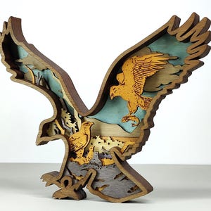 Op de afbeelding: Een gelaagde houten sculptuur van een vliegende adelaar, met uitgestrekte vleugels. De sculptuur heeft een gedetailleerd ontwerp met meerdere lagen, met de adelaar in tinten bruin, geel en blauw. Het kunstwerk is een decoratief stuk.