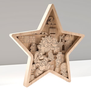 Puede incluir: Adorno de pared de madera con forma de estrella que presenta escenas cortadas con l&aacute;ser de la serie de videojuegos Super Mario. La obra de arte incluye personajes como Mario, Bowser, la Princesa Peach y Toad, junto con elementos ic&oacute;nicos.
