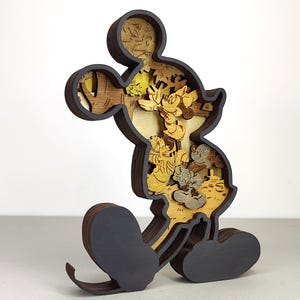 Puede incluir: Una figura de madera de Mickey Mouse con un diseño en capas. La figura es principalmente marrón y gris, con escenas interiores en amarillo y beige. La figura está de pie, con sus icónicas orejas grandes y pies redondos. El diseño en capas crea un efecto 3D.