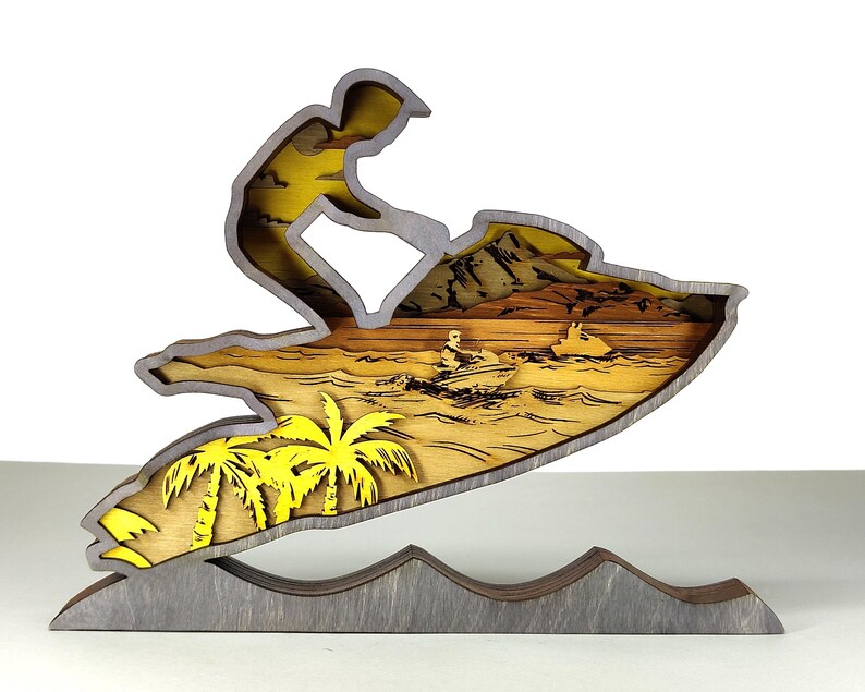 Pu&ograve; includere: Scultura in legno a strati raffigurante una persona che fa jet ski. La scultura presenta palme gialle, un cielo giallo e una base grigia. La moto d'acqua &egrave; grigia con interni gialli e l'acqua &egrave; un mix di giallo e marrone.