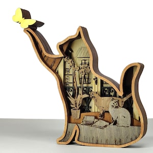 May include: Wooden cat-shaped ornament with a yellow butterfly on its paw. The layered design inside shows a cat, books, plants, and a building. The ornament is made of light and dark brown wood, and is a decorative item.