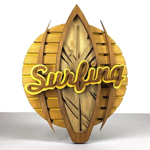 May include: Wooden wall art featuring a surfboard design with the word "Surfing" in yellow and brown. The surfboard is set against a circular background with horizontal wooden slats. The overall design is a warm, natural color.