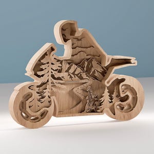 May include: Wooden motorcycle sculpture with a layered design. The sculpture features a rider, mountains, trees, and a winding road. The motorcycle's wheels and body are intricately carved, showcasing a detailed landscape scene.