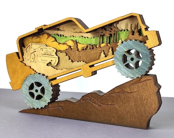 May include: A wooden, layered sculpture of a jeep climbing a mountain. The sculpture features a detailed landscape with trees, mountains, and a jeep design. The wheels are light blue, and the overall color scheme is natural wood tones.