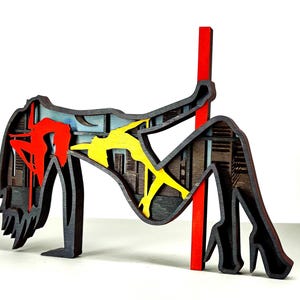 Puede incluir: Escultura de madera en capas que representa una figura bailando en barra. La escultura presenta una barra roja, y la figura está resaltada en rojo y amarillo. El fondo muestra un paisaje urbano.