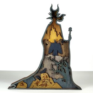 Puede incluir: Silueta de madera multicapa de un personaje con un bast&oacute;n, con un castillo, un cuervo y otros elementos. La pieza es principalmente marr&oacute;n, gris y dorada, con intrincados detalles recortados. El dise&ntilde;o general es una representaci&oacute;n art&iacute;stica estilizada.