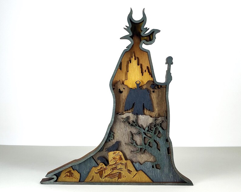 Puede incluir: Silueta de madera multicapa de un personaje con un bast&oacute;n, con un castillo, un cuervo y otros elementos. La pieza es principalmente marr&oacute;n, gris y dorada, con intrincados detalles recortados. El dise&ntilde;o general es una representaci&oacute;n art&iacute;stica estilizada.