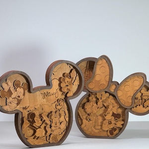 Könnte beinhalten: Zwei Wandkunstwerke aus Holz zum Thema Disney. Eines ist der Kopf von Mickey Mouse, das andere ist der Kopf von Minnie Mouse. Jedes Stück hat geschichtete Designs mit Disney-Figuren und dem Wort "Mickey". Das Holz hat eine natürliche Oberfläche.