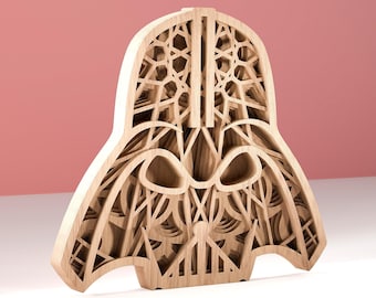 May include: A wooden, layered sculpture of Darth Vader's helmet. The light-colored wood is intricately cut to create a detailed, three-dimensional effect. The sculpture is set against a pink background.